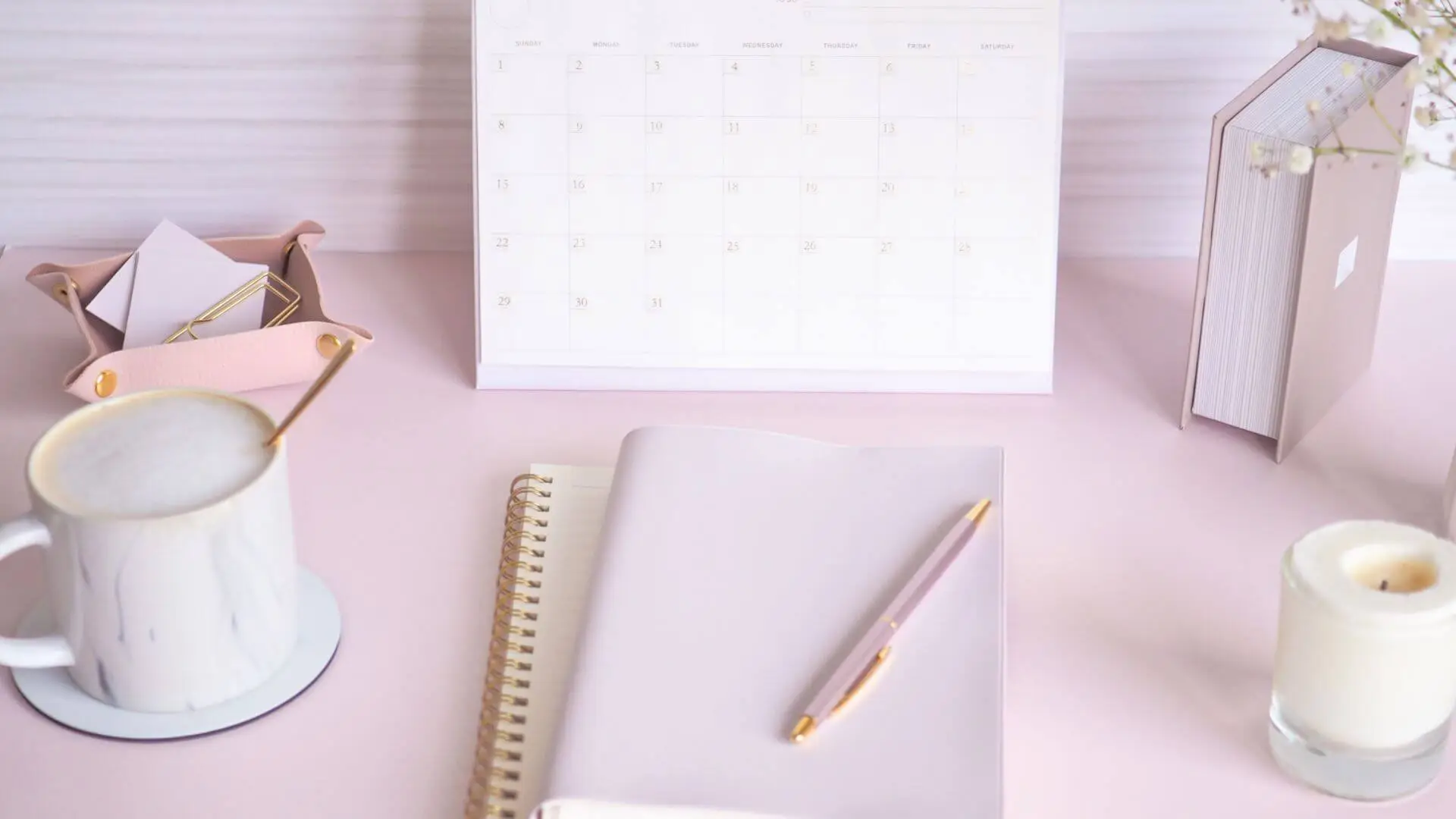 Minimal workspace with neutral tones featuring a calendar, notebook, pen, coffee mug, and candle – cozy and organized planning setup
