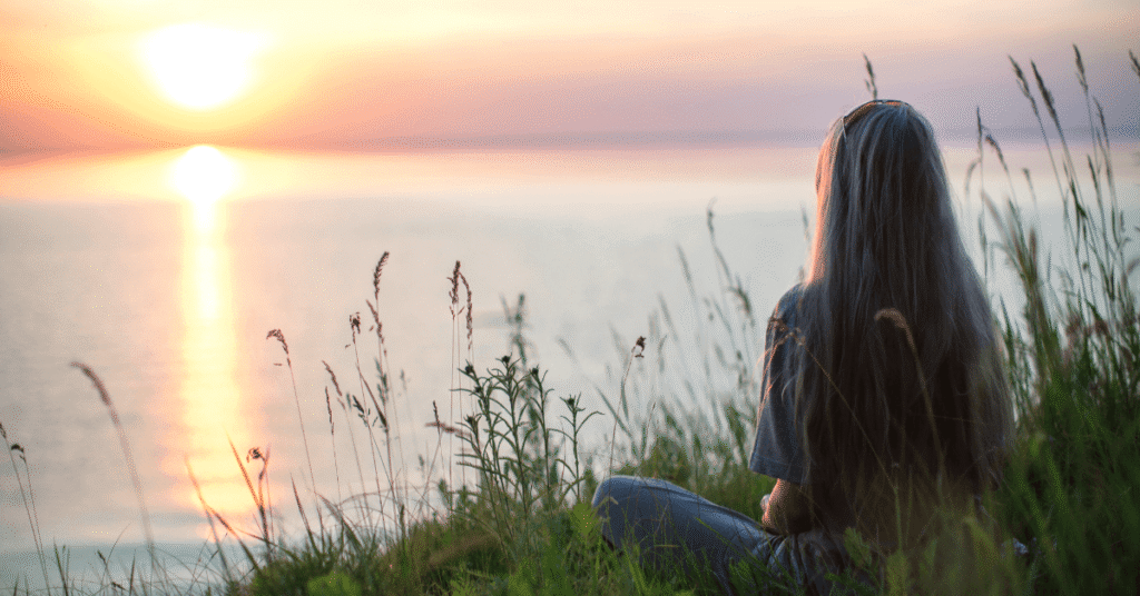 Woman watching a peaceful sunrise by the lake while praying for peace during anxiety, worry, fear, and overthinking.