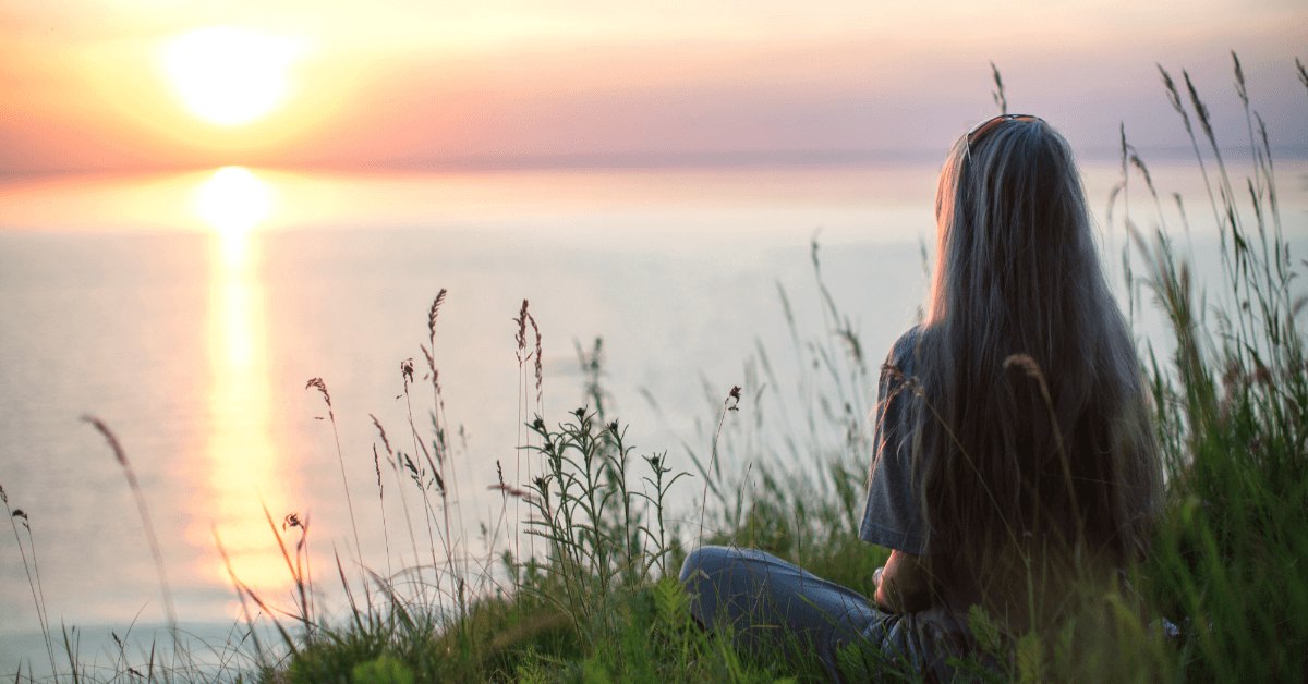 Woman watching a peaceful sunrise by the lake while praying for peace during anxiety, worry, fear, and overthinking.